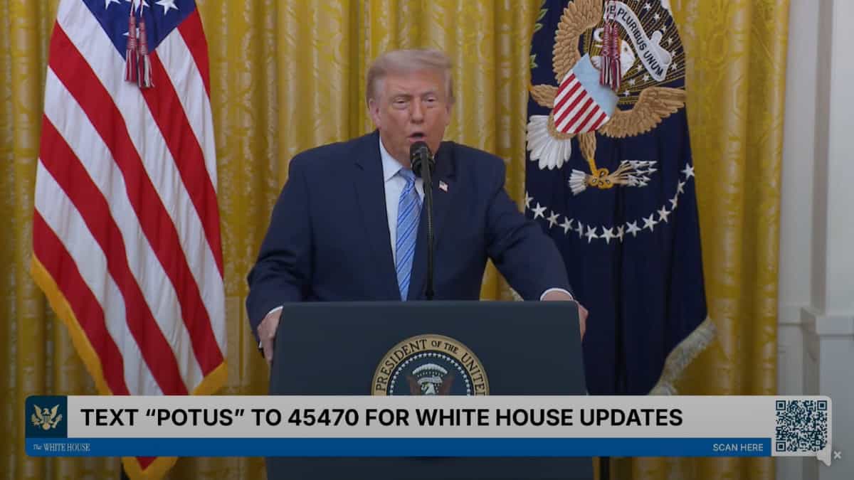 Donald Trump en conferencia con fondo de cortinas doradas y bandera de EE. UU. — memphisnoticias.com